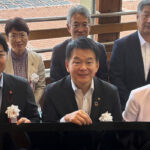ペロブスカイト太陽電池のフィルムを持つさいたま市の清水勇人市長（手前中央）と 環境省の森下千里政務官（手前右）。奥は実際に設置された電池