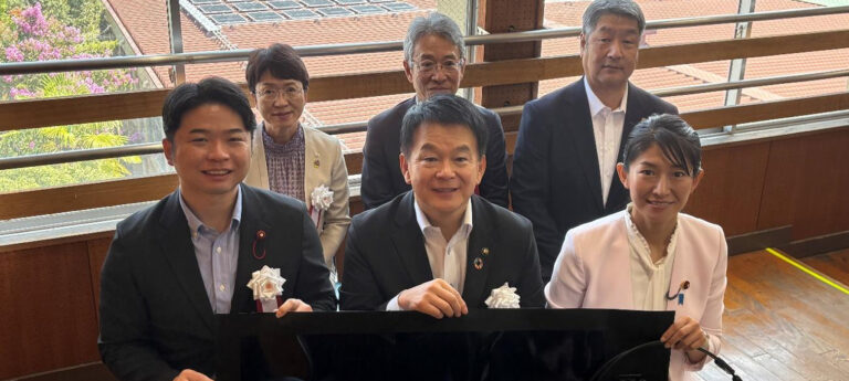 ペロブスカイト太陽電池のフィルムを持つさいたま市の清水勇人市長（手前中央）と 環境省の森下千里政務官（手前右）。奥は実際に設置された電池